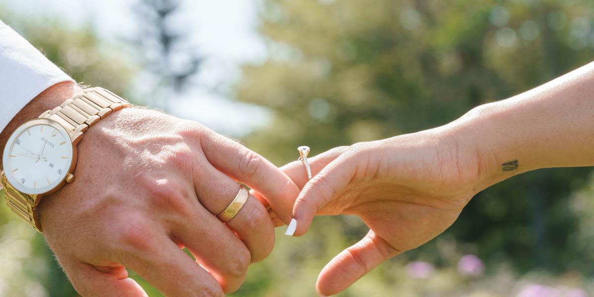Close-up of men and women's hands wearing a wedding band and engagement ring.