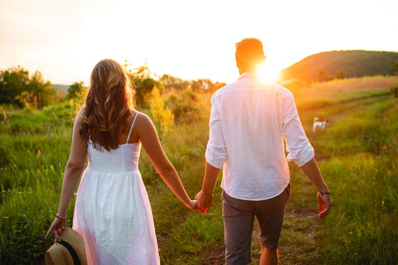 Couple holding hands walking into sunset 