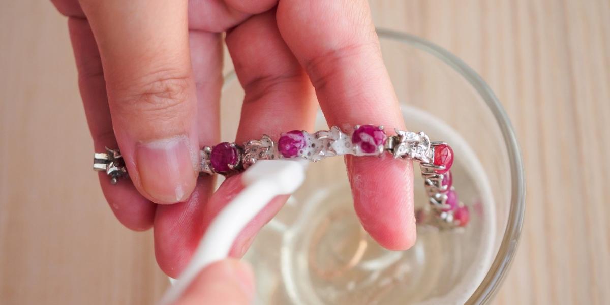 Hand cleaning gemstone bracelet with brush and soapy water for daily jewellery maintenance.